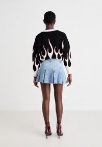Svart og hvit genser med rødt flamme-design, kombinert med en lys blå denim plissert skjørt. Modell iført burgunder ankelstøvler.