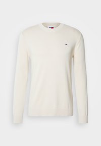 Pull en maille couleur crème à manches longues, col rond et petit logo Tommy Hilfiger sur le côté gauche de la poitrine.