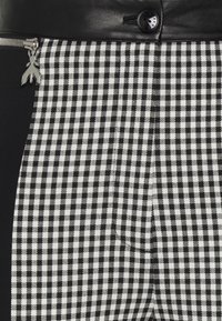 Zwart-witte geruite broek met een leren tailleband, een zak met ritssluiting en zilverkleurige accenten.