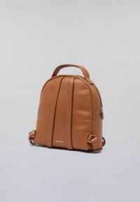 Mochila de cuero marrón con forma redondeada, que presenta detalles de costura vertical, un asa en la parte superior y correas laterales ajustables. Cierre con cremallera.