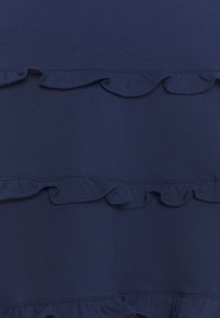 Mörkblått tyg med volangdetaljer. Ytan är slät och volangerna är lager på lager, vilket skapar ett vågigt mönster över materialet.