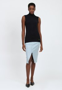 Top a manica lunga nera senza maniche abbinata a una gonna di jeans azzurra chiara con uno spacco frontale. Il modello indossa tacchi a punta neri.