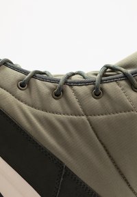 Olivengrøn sneakers detalje med quiltet stof, sorte accenter, metaløjer og teksturerede snørebånd. Glat og polstret overfladetextur.