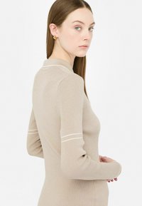 Maglione lungo beige a coste con colletto polo e linee bianche lungo le spalle. Texture morbida e design aderente.