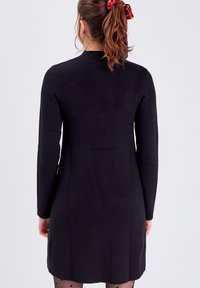 Robe en maille noire à manches longues, coupe droite et col côtelé. Elle présente une texture lisse et tombe à mi-cuisse.