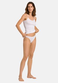 Top in cotone bianco senza maniche con spalline sottili e mutandine in stile bikini bianche coordinate. Design semplice e texture liscia. Posizione a piedi nudi.