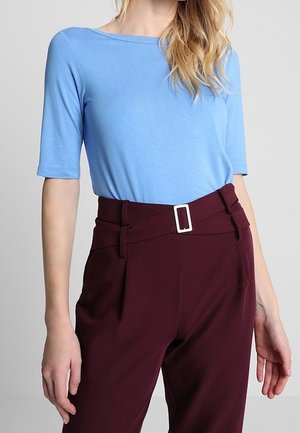 Jasnoniebieski top z krótkim rękawem i dekoltem w szpic, zestawiony z bordowymi, wysokim stanem spodniami z białą prostokątną klamrą i zakładkami.