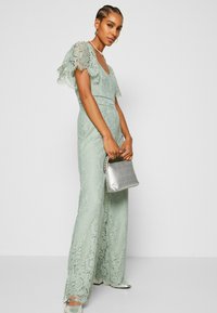Spetsbyxdress i mintgrön med korta, utsvängda ärmar, vida ben och intrikata blommönster. Matchad med en silverclutch och skor.
