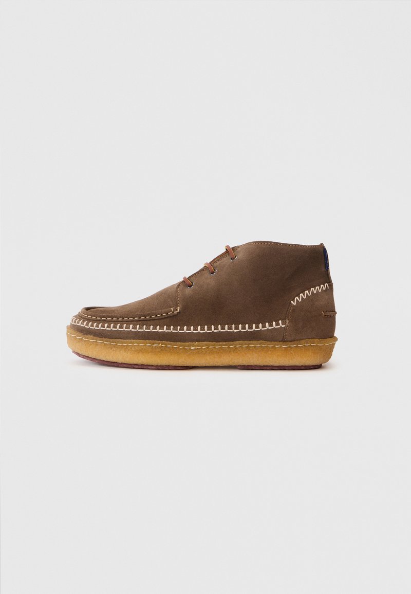 Bottine en suede marron avec un bout arrondi, des coutures contrastantes et une semelle en caoutchouc gomme. Elle dispose de deux paires d'œillets pour les lacets.