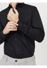 Czarna koszula z guzikami, klasyczny kołnierz, długie rękawy i zapięcia na guziki w mankietach, w zestawie z jasnoszarymi spodniami o fakturowanej tkaninie.