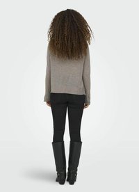 Maglione grigio a maglia con una vestibilità morbida, abbinato a jeans skinny neri e stivali neri al ginocchio con fibbie. Acconciatura texturizzata che supera le spalle.