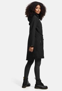 Zwarte waterdichte parka met een kap, voornaam trekkenkoord, twee met rits afgesloten zakken en lange mouwen, gecombineerd met donkere skinny jeans en zwarte laarzen.