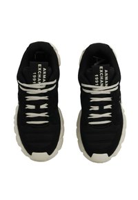 Sneakers neri con suole bianche spesse e lacci bianchi, marchiati "Armani Exchange 1991" sulle etichette nere, viste dall'alto.