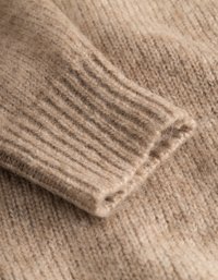 Harmaa neulepuserokangas, jossa on ribbireunat, pehmeä tekstuuri ja lämmin, kevyt ilme hienovaraisilla värieroilla.