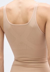 Maiou bej fără cusături, cu bretele late, având un design texturat încrucișat pe spate și o siluetă netedă, care se mulează pe corp.