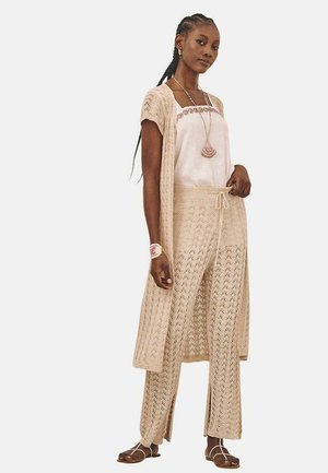 Conjunto de ganchillo en color beige que incluye un cárdigan largo, una blusa suelta y pantalones de pierna ancha, con patrones intrincados y detalles de cordón.