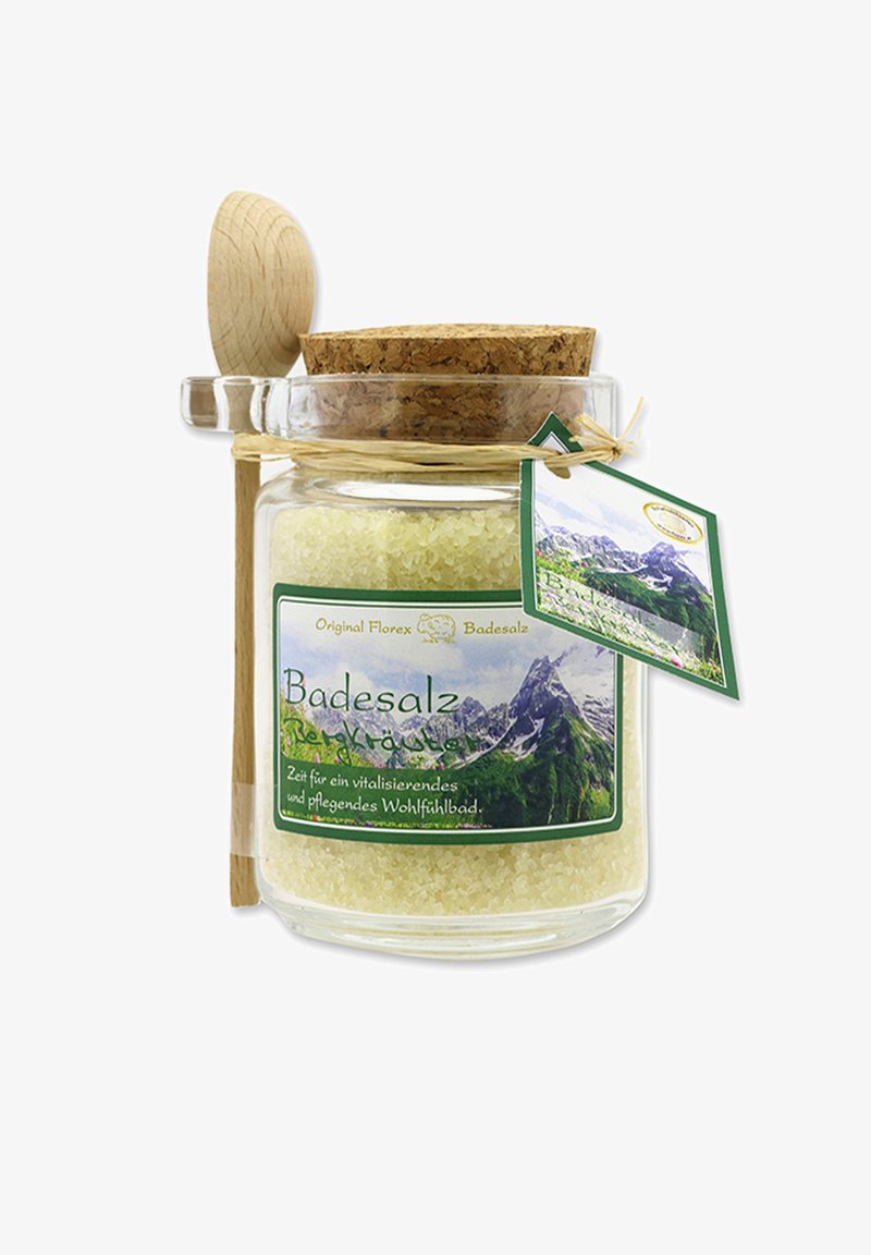 Glass jar of yellow bath salts with cork lid, wooden spoon attached, and green label showing mountains and German text.