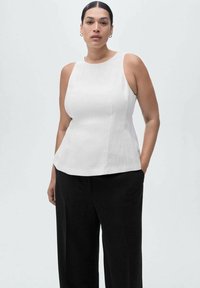 Belo brezrokavnik s krožnim izrezom, s strukturirano obliko in lahkotnim materialom, v kombinaciji s črnimi širokimi hlačami.