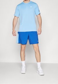 Ljusblå kortärmad träningsskjorta och blå shorts med sidofickor, i kombination med vita sneakers och ankelsockor.