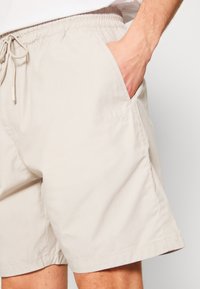 Beige shorts met een elastische tailleband en trekkoord. Voorzien van zijzakken en geborduurd "HUGO" logo op de linker heup. Soepele stofstructuur.