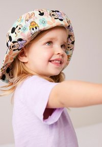 Cappello a secchiello per bambini con personaggi dei cartoni animati in colori pastello, dotato di un orlo morbido e tessuto soffice. Il bambino indossa una maglietta di colore viola chiaro.