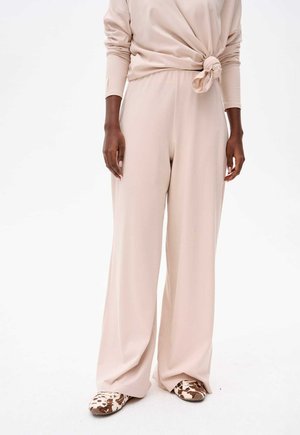 Hellrosa weit geschnittene Hosen aus weichem Stoff mit einem geknoteten Taillendetail. Kombiniert mit gemusterten Schuhen in neutralen Tönen.