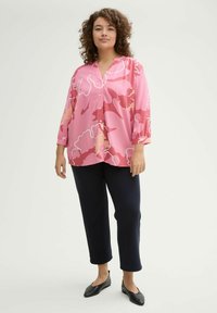 Blouse rose avec motif floral abstrait, devant boutonné et manches trois-quarts. Associée à un pantalon noir cropped et des ballerines noires.