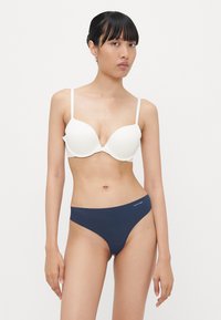 Vit vadderad bh med justerbara band, i kombination med mörkblå hipsterbriefs. Båda plaggen har en slät yta och minimal detailing.
