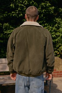 Chaqueta de pana en verde oliva con un cuello de borreguillo blanco, con un corte relajado y puños acanalados. Combinada con jeans de denim azul claro.