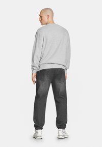 Szara bluza z ściągaczami przy mankietach i u dołu, w połączeniu z ciemnoszarymi dżinsami. Model odwrócony plecami, prezentujący luźny krój i długość do kostek.