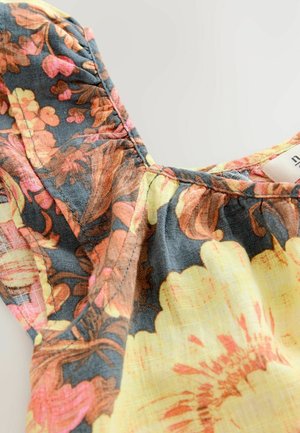 Blommönstrad topp i ett lättviktigt tyg. Har detaljer med rynkade sömmar, en mörk blågrå bakgrund och accenter av gult, orange och rosa.