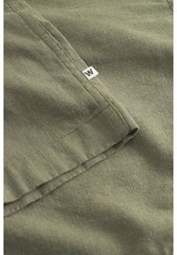 Tissu vert olive avec une surface texturée, présentant un bord replié et une petite étiquette blanche avec la lettre "A".