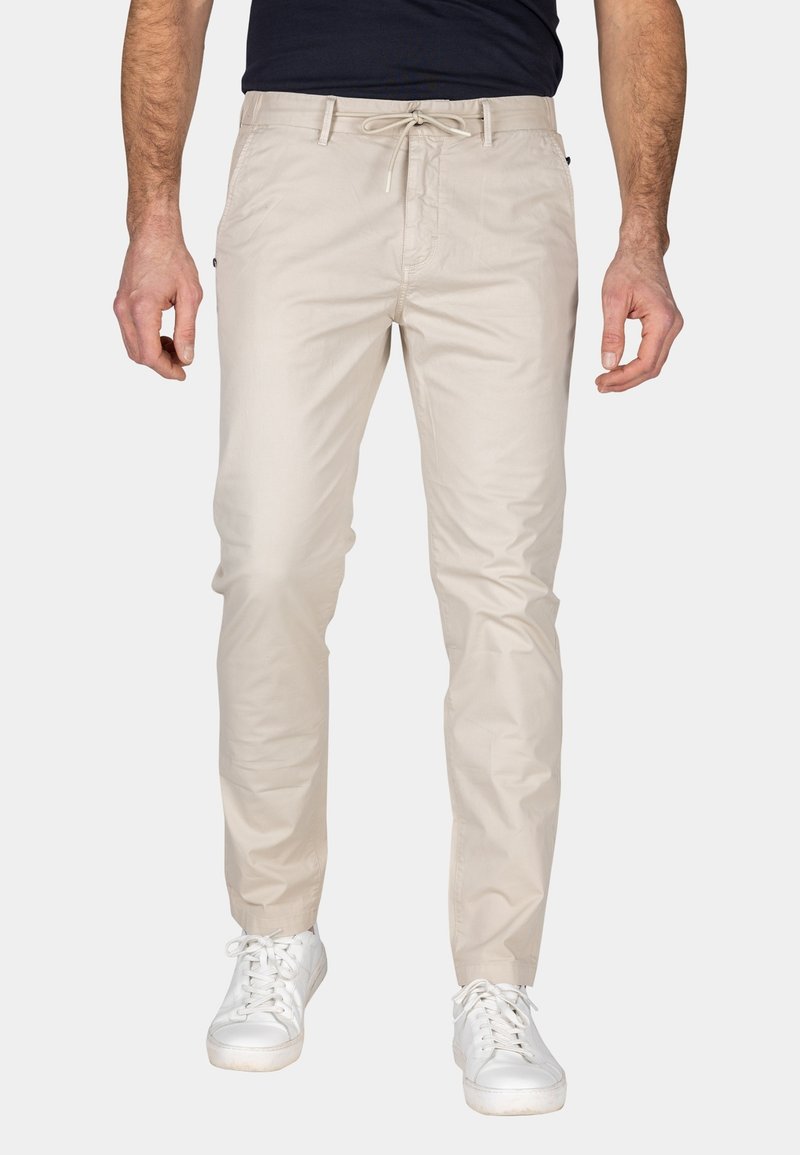 Beige katoenen broeken met een trekkoord rond de taille, slim fit, zijzakken en een gladde textuur, gecombineerd met witte sneakers.