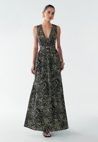 Maxime dress in musta avec un design à motif en vagues vertes, décolleté en V profond, taille cintrée et tissu fluide. Accentué par des accessoires en or.