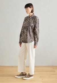 Leopardmønster, skjorte med krage og lange ermer, kombinert med kremfargede vide bukser og matchende leopardmønstrede slipsko.
