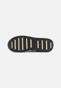 Suola di scarpa in gomma nera con un palmo distintivo e accenti beige. Presenta scanalature orizzontali per una migliore aderenza e durata. Logo visibile.