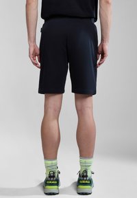 Pantalones cortos navy de tejido suave, con un corte relajado y cinturilla elástica. Combinados con zapatillas deportivas verdes y grises y calcetines verde claro.