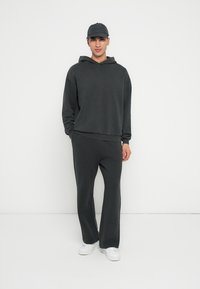 Dunkelgrauer Hoodie mit einer Fronttasche, kombiniert mit passender, locker sitzender Hose; beide aus weichem Stoff gefertigt. Weiße Sneakers runden das Outfit ab.