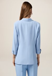 Lichtblauwe op maat gemaakte blazer met driekwartmouwen, een geknipt kraag en opgerolde mouwen, met een gladde textuur en gestructureerde silhouet.