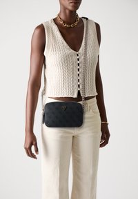 Sac en cuir noir à bandoulière avec une surface texturée, accent logo triangulaire et une chaîne en argent. Portez-le avec un haut en tricot crème et un pantalon beige.