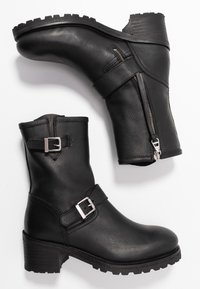 Černé kožené kotníkové boty se stříbrnými detaily. Obsahují boční zip, robustní podešev a dvě nastavitelné pásky v horní části.