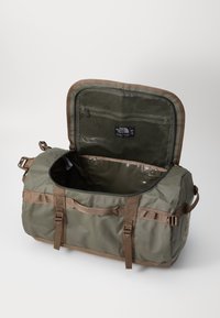 Dufflebag i olivengrønn stoff med brune stropper. Har en bred åpning, mesh-lomme inni, og en vanntett fôr.
