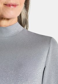Maglione a collo alto grigio scintillante caratterizzato da un design aderente e liscio, con un alto colletto e una superficie morbida e testurizzata che presenta una leggera lucentezza.
