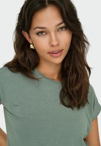 Maglietta khaki verde a maniche corte con una trama a costine e sottili dettagli metallici. Presenta un collo rotondo e una vestibilità comoda.