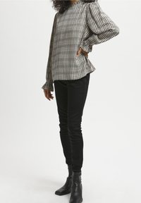 Schwarz-weiße karierte Bluse mit langen Ärmeln und Rüschensäumen, kombiniert mit schwarzen Slim-Fit-Jeans und Stiefeletten.