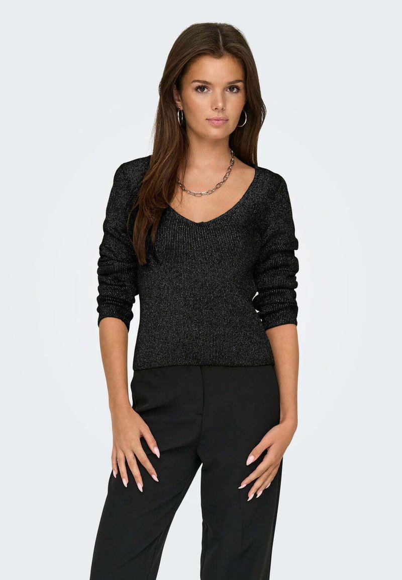 Maglione nero a maglia con scollo a V, maniche lunghe e texture a costine. Indossato con pantaloni neri, abbinato a una collana con catena d'argento.