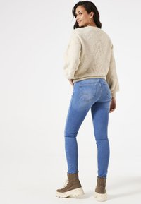 Crèmekleurige gebreide trui met geribbelde zoom, gecombineerd met blauwe skinny jeans. Model draagt bruine veterschoenen met dikke witte zolen.