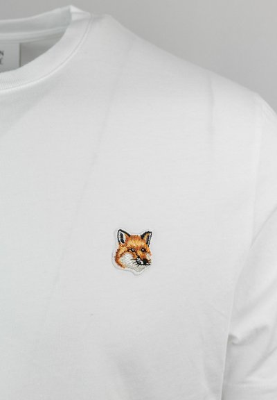 T-shirt bianco in cotone con un piccolo e dettagliato ricamo di una testa di volpe in arancione e nero, posizionato sulla parte sinistra del petto.