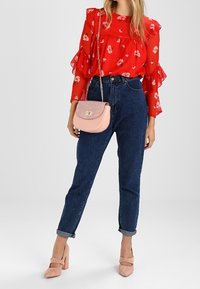 Czerwona bluzka w kwiaty z falbanami na rękawach, ciemnoniebieskie jeansy z wysokim stanem, jasnoróżowa torebka crossbody oraz beżowe buty na słupku.