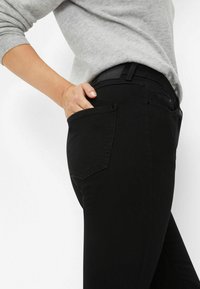 Jeans noirs au design ajusté, avec des poches avant et arrière et une texture subtile. Taille mise en valeur avec une étiquette à l'arrière.